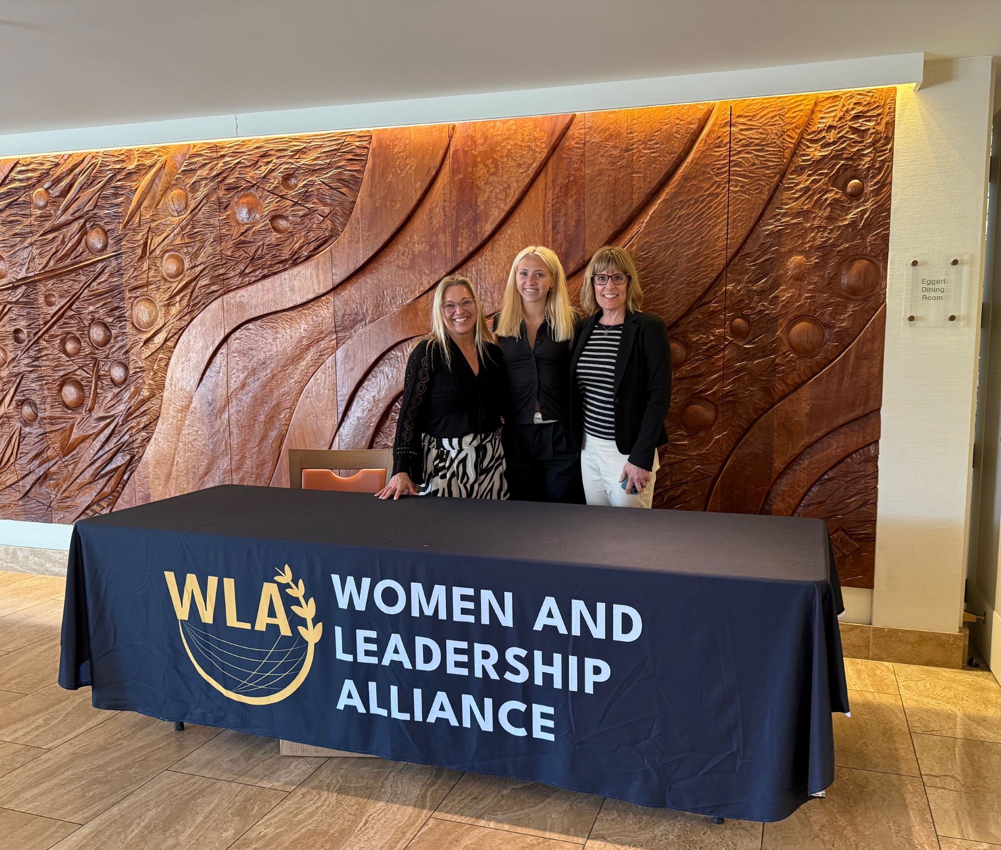 Photo with Izzy and Beth Murphy standing in front of the Women and Leadership Alliance Table at the Atheneum
