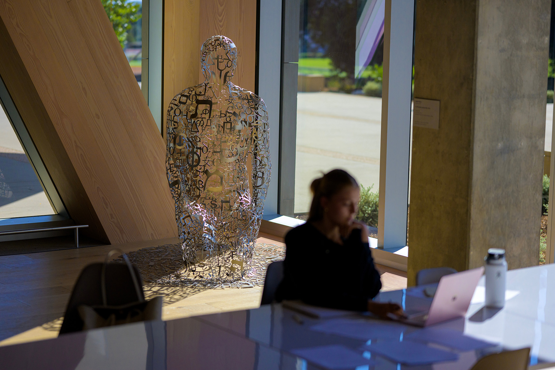 Jaume Plensa's sculpture in the background with a student seated at a table in the foreground.