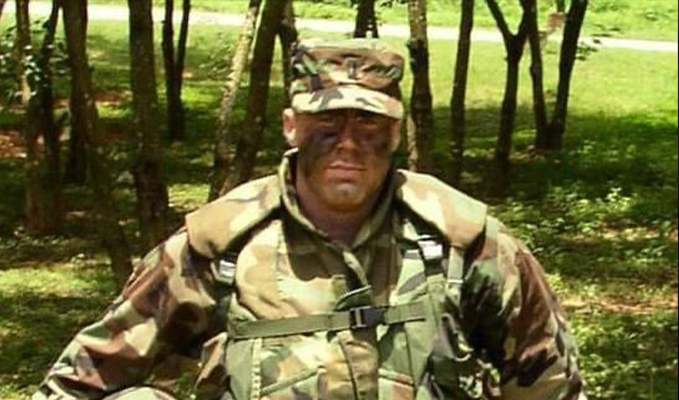 Man wearing military uniform standing outside in open grass field.