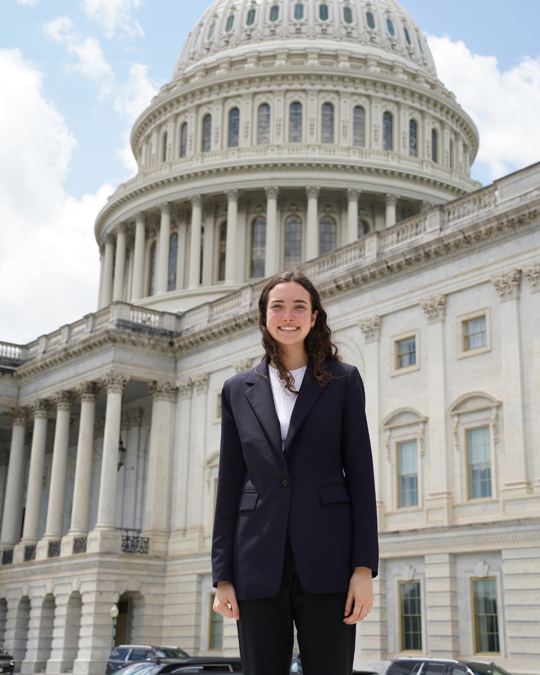 Girl wearing black suit with brown wavy hair standing in front of White House.