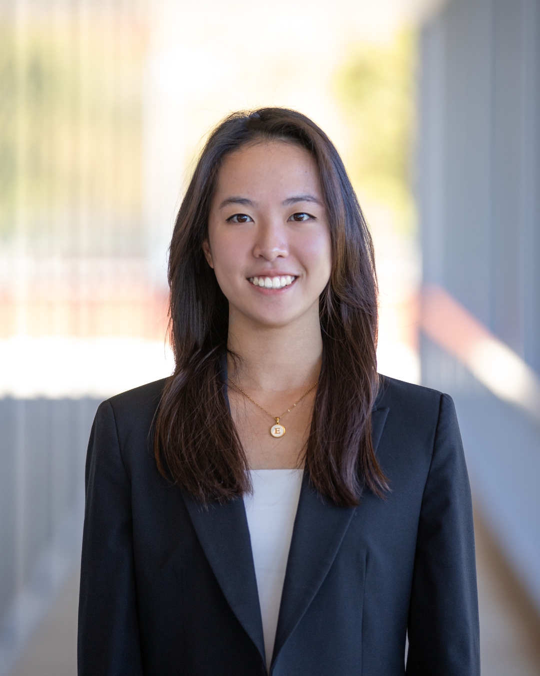 Girl standing in front of walkway wearing navy blazer with white shirt and long black hair.
