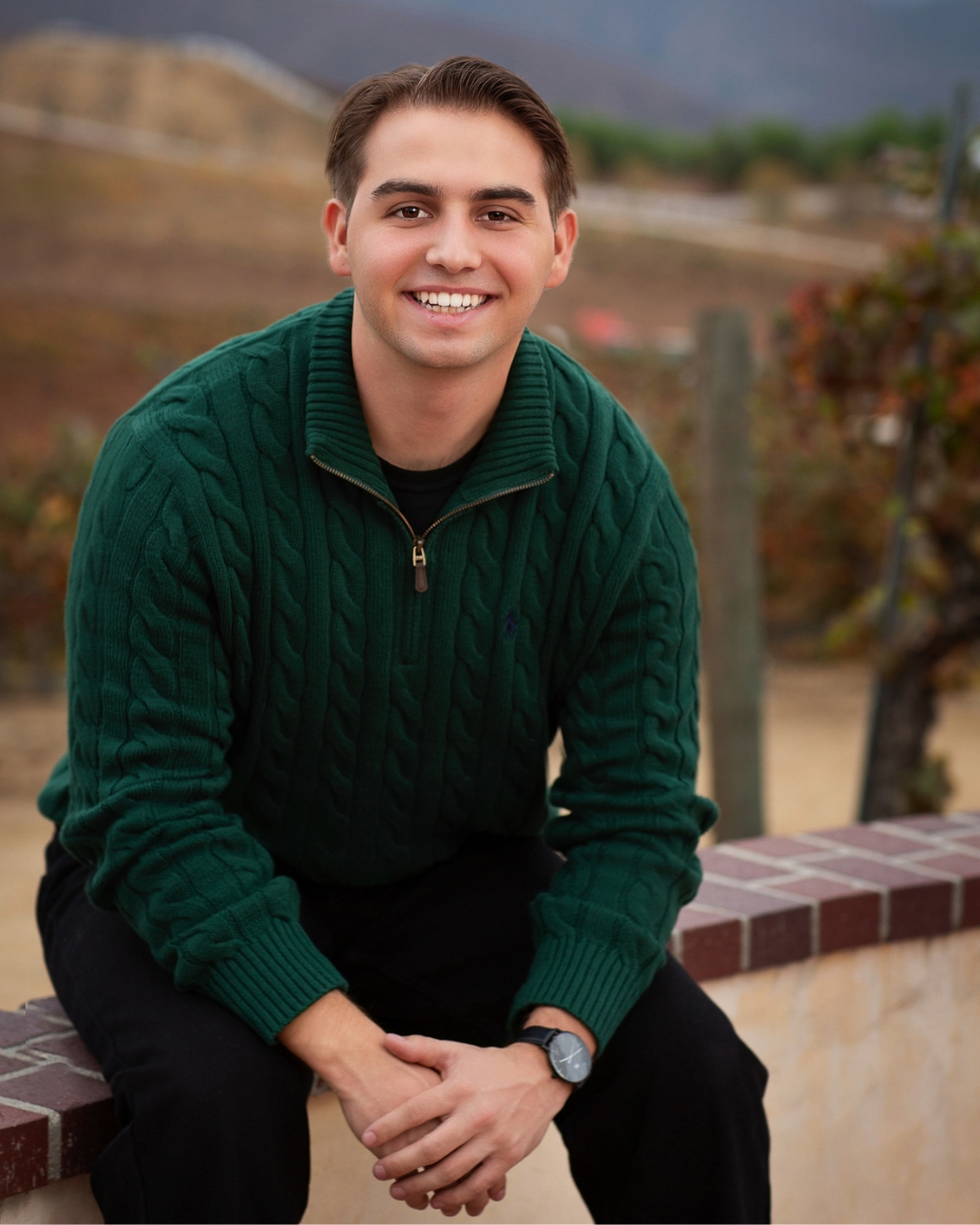 Man in green sweater with short brown hair sitting on bench. 