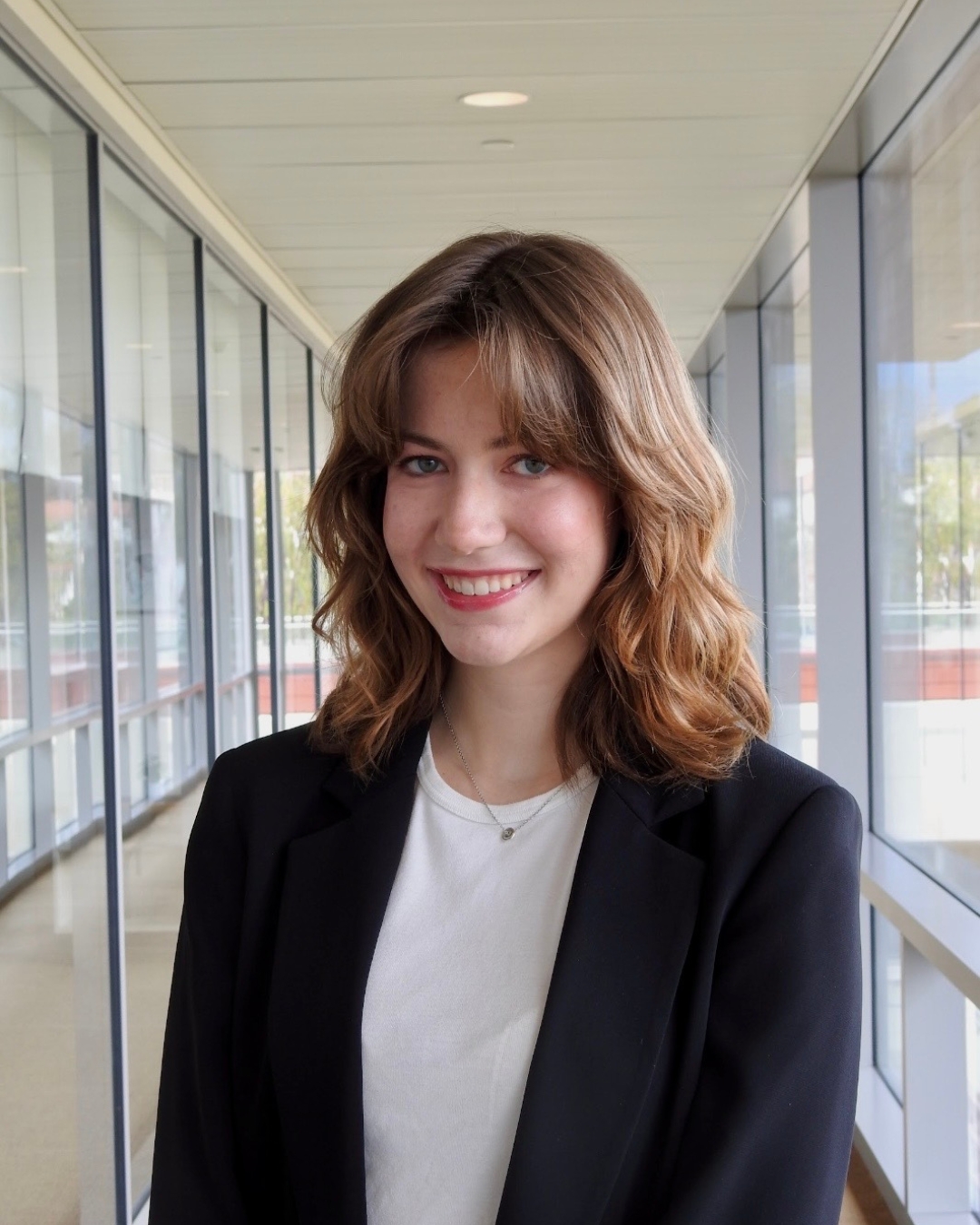 Girl with black blazer and white top with short brown curly hair.