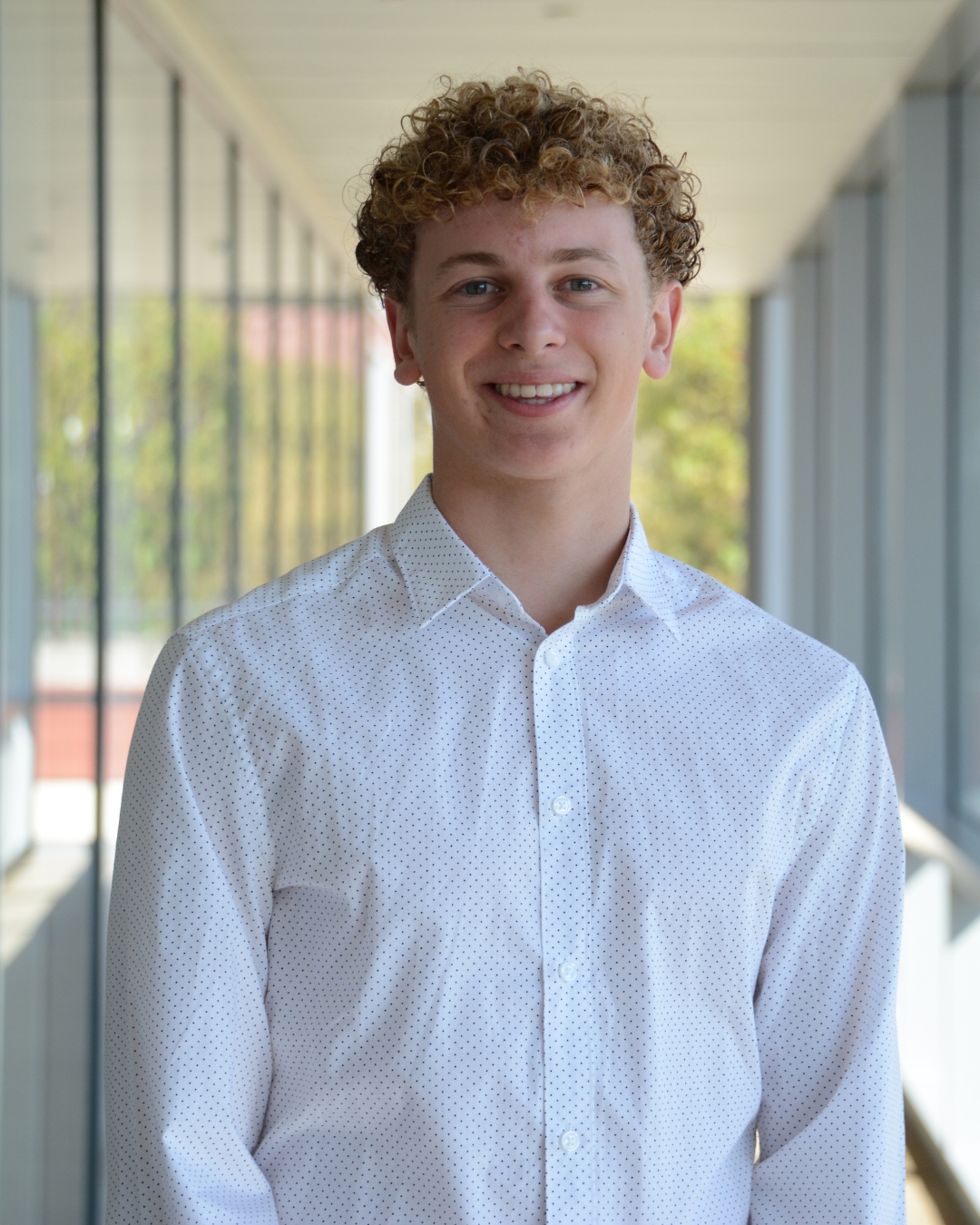 Man with white long sleeve and short blond curly hair standing in front of walkway.