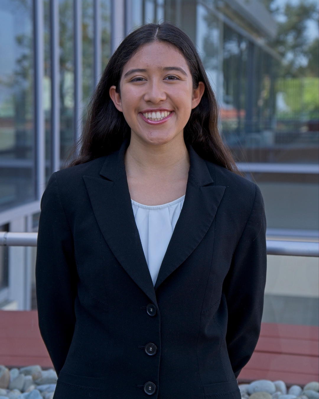 Girl standing in front of CMC walkway wearing black blazer with long brown hair.