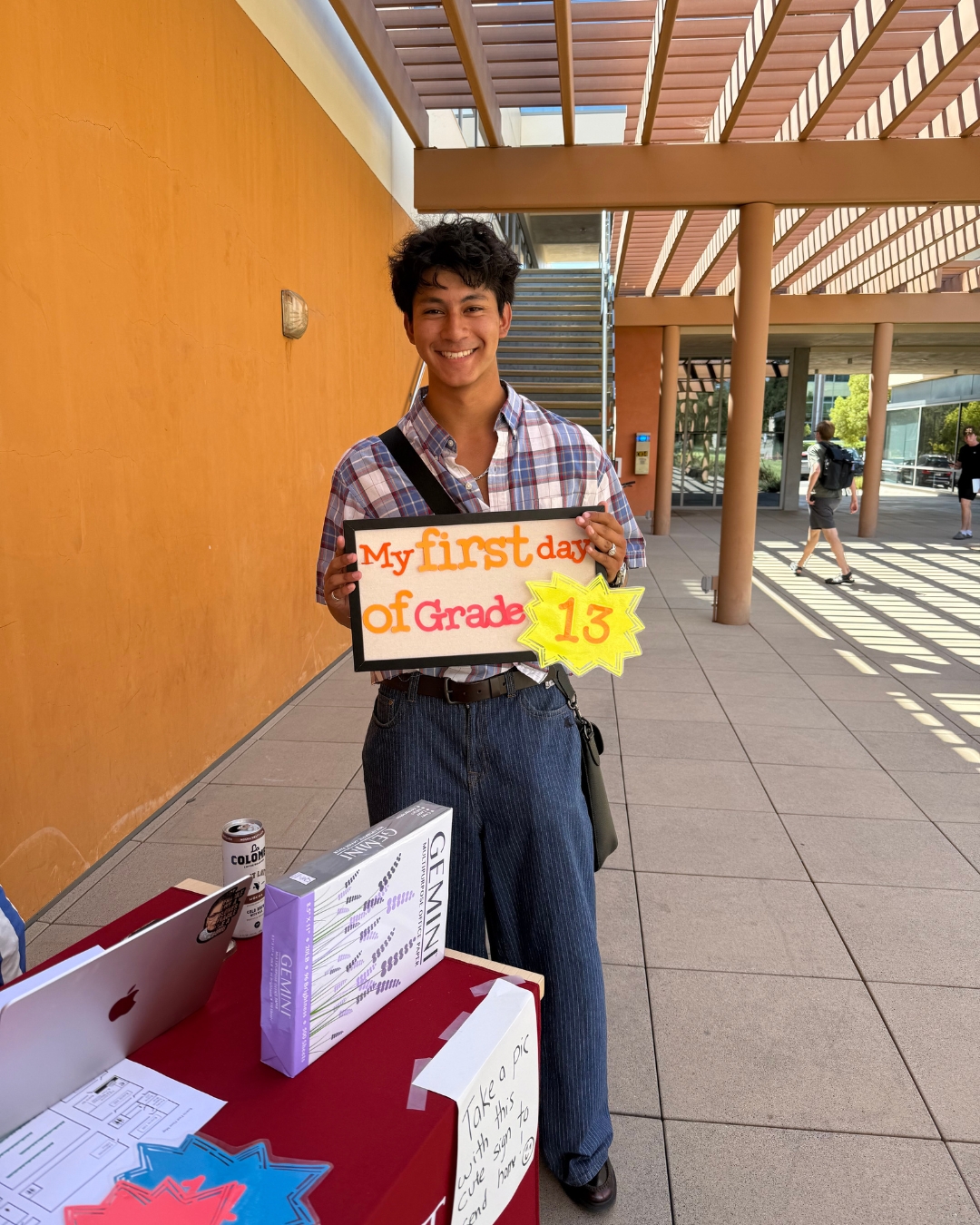 Man with flannel and jeans holding yellow sign that reads "my first day of grade 13."