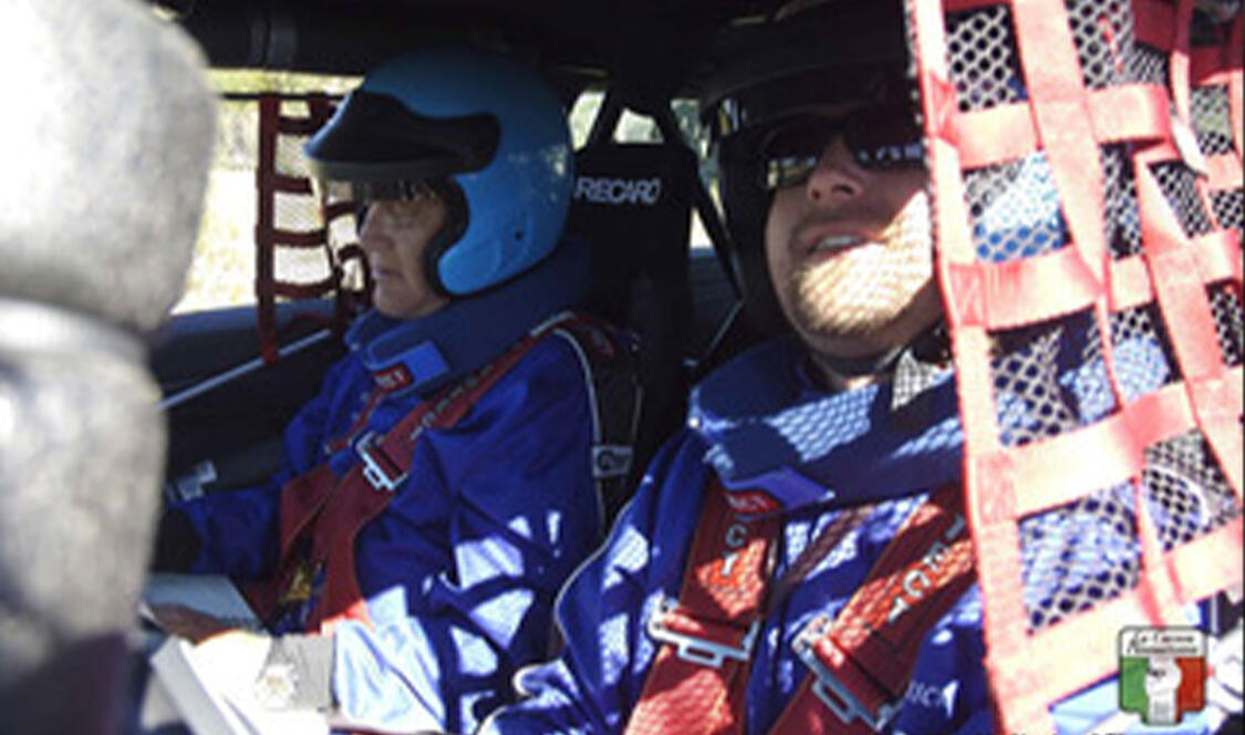Two men inside racing car with racing gear and helmet.