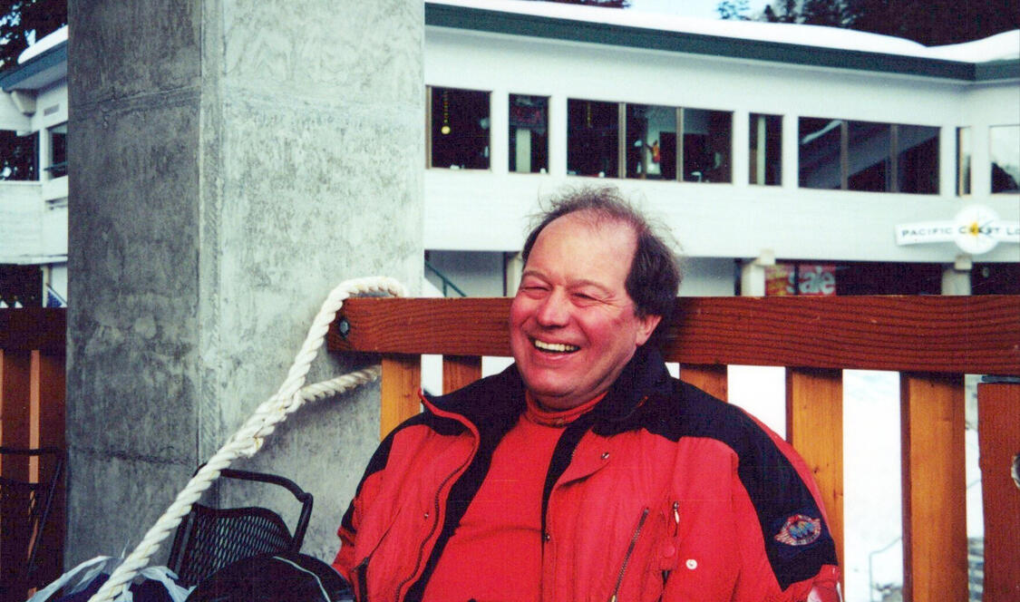 Man sitting on bench wearing red jacket with black short hair.