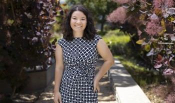 Kimiko Adler ’23 poses for a photo by a flowering bush on campus
