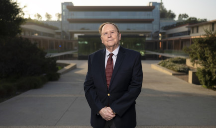 A suited up Professor Frederick Lynch stands smiling in the California sun in front of the Kube and Kravis Center.