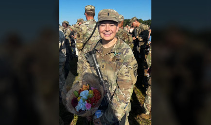 Lauren Jeans '24 in military fatigues holds a rifle and bouquet of flowers.